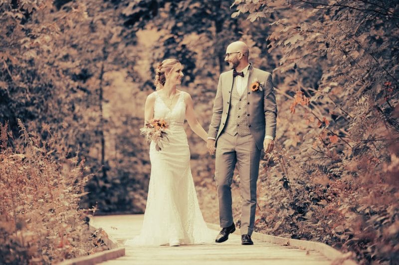 Braut und Bräutigam Hand in Hand auf einem Waldweg bei ihrer Hochzeit in Wildhaus, fotografiert von Adrian Flütsch.